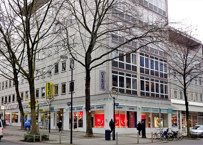 Large building with stores on the ground floor, trees and pedestrians