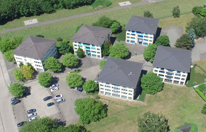 five multi-family houses from bird's eye view, green areas around, cars on parking lot
