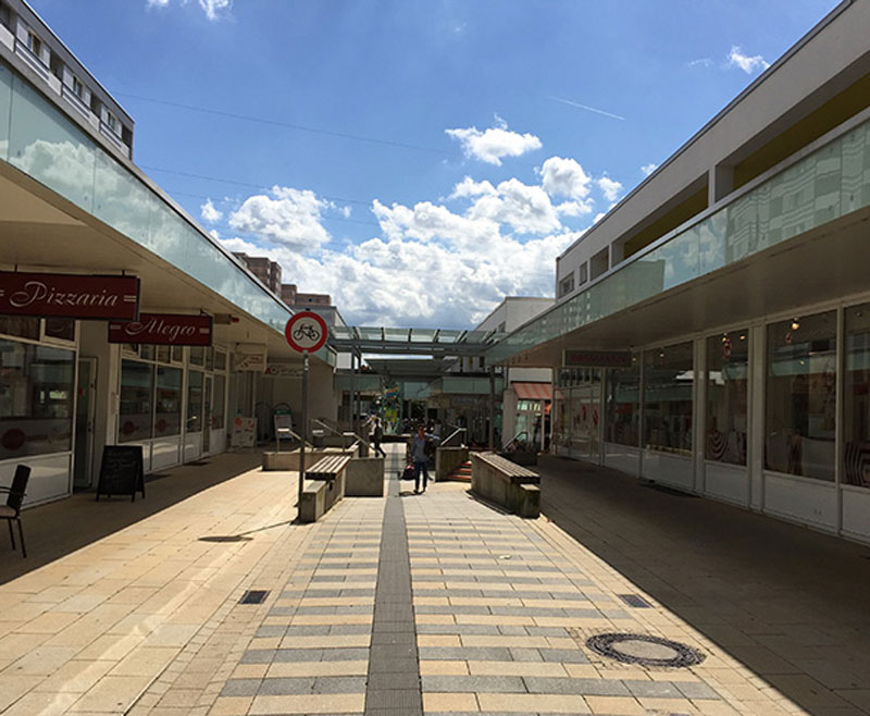 Einzelhandel und Gastronomie einer leeren Einkaufsstraße, blauer Himmel mit Wolken